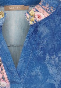 Denimöverdel med djup V-ringning och blommöster på kragen. Tyget är texturerat med ett blårandrande mönster. Storleksetikett: S/M.