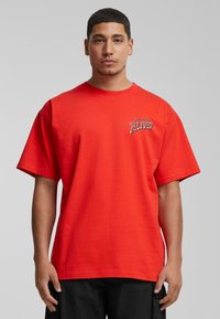 Rød bomulds T-shirt med rund hals og korte ærmer. Har et grafisk print "ZOO YORK ALIVE!" på venstre bryst.