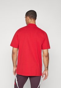 Rød bomulds T-shirt med korte ærmer, rund halsudskæring og en løs pasform. Har en glat tekstur og dobbelt syning i kanten.
