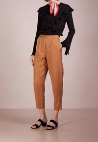 Svart långärmad topp med volanger; tan tapered byxor med fickor; svarta sandaler med två remmar; röd halsduk med vitt mönster runt halsen.