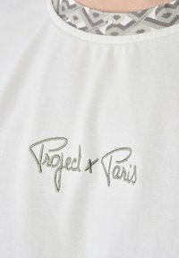 Camiseta de algodón blanca con un cuello redondo, interior con un patrón geométrico y logo bordado "Project x Paris" en plata.