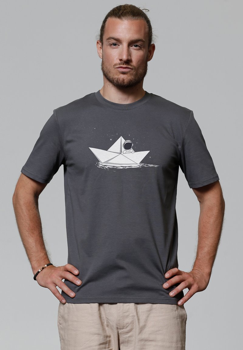 Grijze t-shirt met korte mouwen, voorzien van een witte afbeelding van een papieren boot met een astronaut, tegen een lichtgrijze achtergrond.