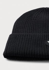 Black ribbed knit beanie with folded cuff and small circular logo patch on a light background.