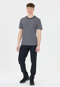 Námořnické a bílé pruhované tričko s krátkým rukávem, doplněné o těsné černé kalhoty a černé turistické boty, stojící na hladkém pozadí.