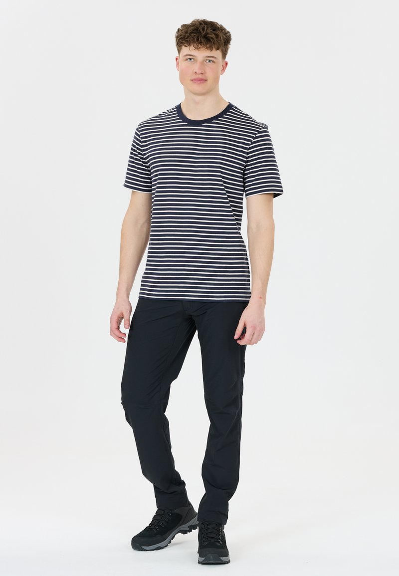 Námořnické a bílé pruhované tričko s krátkým rukávem, doplněné o těsné černé kalhoty a černé turistické boty, stojící na hladkém pozadí.