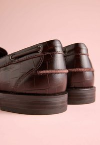 Pantofi maro închis din piele cu textură de crocodil, cu ochiuri metalice și toc jos din cauciuc. Vedere din spate ce evidențiază detaliile cusăturii.