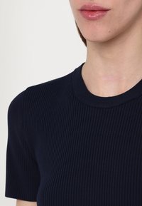 Gros plan d'une personne portant un haut côtelé bleu marine à manches courtes, montrant l'encolure et le bas du visage avec des lèvres brillantes.
