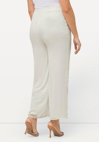 Lichtbeige wijde broek met elastische tailleband, een gladde textuur en een ontspannen pasvorm, gecombineerd met gesflesde hoge hakken.