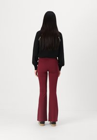 Pantalons flared bordeaux taille haute avec un design épuré, associés à un haut noir à manches longues, présentés de dos.