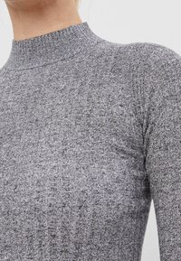 Szary prążkowany sweter dziany z wysokim kołnierzem. Materiał jest miękki i dopasowany, z widocznymi pionowymi liniami na tkaninie.