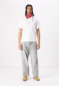 Tricou alb cu logo, blugi călduroși gri și adidași bej. Bandiță roșie în jurul gâtului. Păr drept cu împletituri.