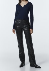 Marinblå ribbat stickad tröja med V-ringning, kombinerad med högmidjade svarta läderbyxor. Slim fit, slät textur och minimala sömmar.