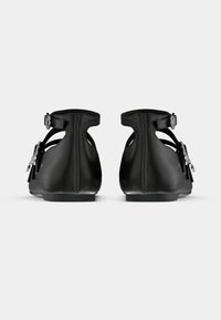 Sandalias negras de cuero con cierre de hebilla, laterales abiertos y suela plana. Textura suave con detalles mínimos de herrajes.