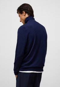 Navyblauem Pullover mit hohem Kragen, aus weichem Material gefertigt. Verfügt über lange Ärmel und einen lockeren Schnitt, mit minimalen Nähdetails.
