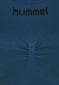 Blå trenings-topp laget av teksturert stoff med en samlet design i midten og en svart logo trykket på halsen.