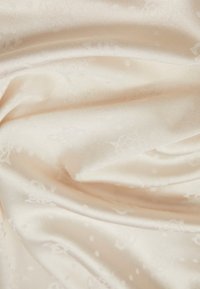 Tissu satin crème pâle avec une texture lisse, présentant de subtils motifs floraux et un éclat délicat, tombant en douces plis.