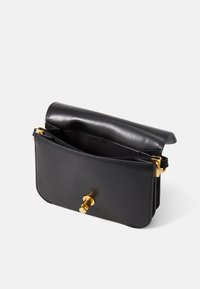 Bolsa de mão de couro preto com detalhes em metal dourado, apresentando um fecho de aba e um interior aberto para armazenamento. Textura suave e forma retangular.