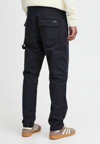 Navy cargo pants with multiple pockets, slim fit, and durable fabric; worn with gray and white striped sneakers. Accent stitching visible.