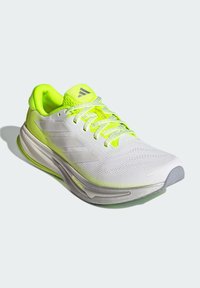 Weißer Laufschuh mit neongelben Akzenten, Obermaterial aus Mesh, strukturierten Oberflächen und drei grauen Streifen. Verfügt über eine gepolsterte Sohle und Schnürung.
