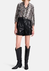 Pantaloni corti neri in pelle a vita alta, camicia a stampa serpente e stivali da cowboy neri al ginocchio con punte affusolate e tacchi robusti.