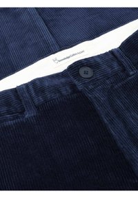 Marineblaue Cordhosen mit Knopfverschluss, markanter gerippter Textur und einem Etikett von Knowledge Cotton Apparel.