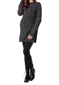 Tunique en tricot noir et blanc à manches longues, dotée de fentes latérales, accompagnée de leggings noirs et de bottes à lacets noires brillantes.