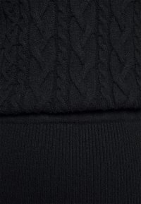Schwarzer Strickstoff mit einem strukturierten Kabelmuster im oberen Abschnitt und einem gerippten Saum am Boden, der ein glattes, harmonisches Design zeigt.
