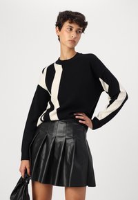 Black and cream striped knit sweater with long sleeves, paired with a black pleated leather skirt. Smooth texture, casual design.