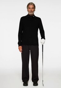 Svart pikétröja med lång ärm, svarta byxor och svarta skor. Håller en golfklubba i ena handen, bär en vit handske på den andra.