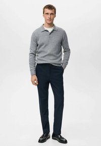 Szary dziany sweter z kołnierzem, zestawiony z ciemnoniebieskimi, dopasowanymi spodniami i czarnymi skórzanymi butami. Prosty design z teksturowanym wykończeniem.