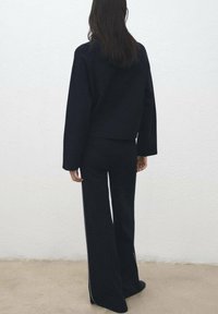 Črn skrajšan pulover in široke hlače, obe iz mehkega pletenega blaga. Hlače imajo stranski trak. Minimalistična zasnova, enobarvna.