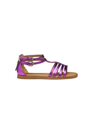 Sandalia gladiadora metálica púrpura con múltiples correas, cierres de hebilla en el tobillo y una suela plana de color marrón. Textura suave, diseño de punta abierta.
