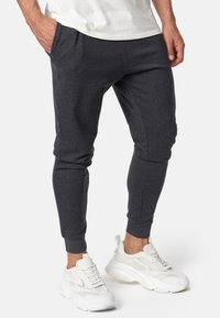 Dunkelgraue Jogginghosen mit Seitentaschen, schmal zulaufenden Beinen, elastischen Bündchen und glatter Textur. Kombiniert mit weißen Sportschuhen.