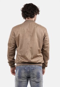 Giubbotto bomber marrone realizzato in un materiale simile alla pelle scamosciata, con polsini e orlo a coste, caratterizzato da un design semplice e pulito, senza decorazioni visibili.