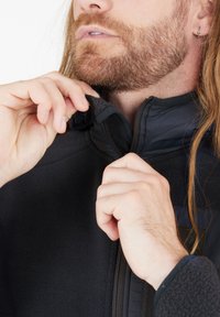 Sort fleecejakke med høj krave, delvist lynlåst. Tekstureret stof, kontrastfyldte glatte panel-detaljer, og et nærbillede af hænder, der justerer kraven.