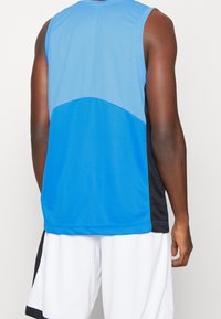 Top sportivo blu in tessuto a rete, con un design morbido e arrotondato per la spalla e pannelli laterali neri.
