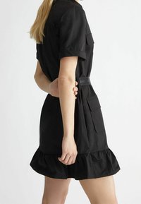 Abito nero con maniche corte, orlo arricciato e vita con cintura. Realizzato in tessuto leggero, con dettagli di tasca a toppa.
