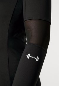 Schwarzes sportliches Langarmshirt mit Mesh-Oberarmpaneelen. Mit einem weißen Logo "NEBBIA" und einem Hantelsymbol am unteren Ärmel. Glatte Textur.