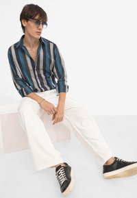 Button-up shirt with navy, teal, and gray stripes, paired with white wide-leg pants and black sneakers with white laces and a worn sole.