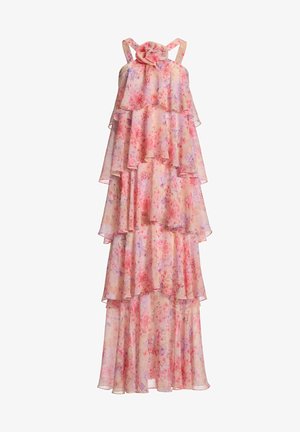 Femme portant une robe maxi rose à fleurs sans manches, à volants, avec un grand détail floral au niveau du décolleté, et des talons argentés ouverts au bout.