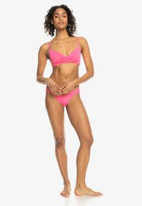 Svijetlo ružičasti bikini set s V-izrezom, tankim naramenicama i donjim dijelom s niskim strukom. Glatka tekstura s minimalističkim dizajnom i bez uzoraka.