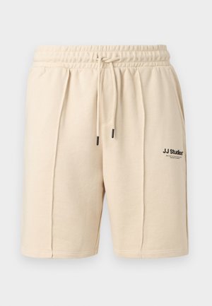 Μπεζ βαμβακερά σορτς με ελαστική μέση και κορδόνι, δύο πλαϊνές τσέπες και μικρό μαύρο λογότυπο "J.J Studios" στο μπροστινό δεξί πόδι.