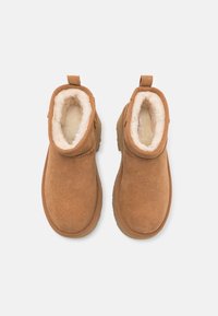 Bottines en daim marron avec doublure en polaire blanche, semelles plates en caoutchouc et languettes à tirer à l'arrière, vues de dessus sur fond blanc.