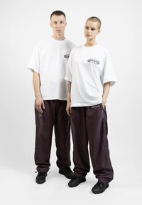 White oversized t-shirts with a black logo, paired with loose maroon pants featuring mesh accents. Black sneakers complete the outfit.