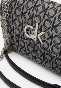 Borsa a mano in tessuto bicolore con motivo, dotata di hardware argentato, che presenta il logo CK, una tracolla a catena e un manico in pelle nera liscia.