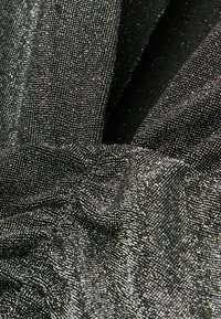 Tela negra con textura y acabado brillante. Presenta intrincados patrones tejidos y pliegues, que reflejan la luz desde distintos ángulos.