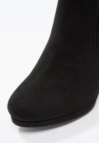 Černé nubukové kotníkové boty s elegantním, špičatým designem a zvýšeným podpatkem. Hladký povrch a minimální akcenty, zaměřující se na elegantní siluetu.
