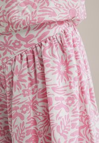 Ziedu raksta audums ar rozā dizainu uz balta fona, kam ir iekrāsota tekstūra viduklī, radot plūstošu siluetu.