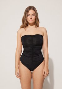 Czarny jednoczęściowy strój kąpielowy bez ramiączek z marszczonym materiałem, tworzącym teksturowany detal na korpusie oraz wysokim krojem nóg. Gładkie wykończenie materiału.