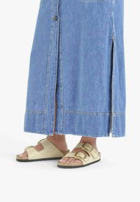 Gonna di denim con spacchi laterali e bottoni, abbinata a sandali bassi beige chiaro con cinturini testurizzati e due fibbie regolabili.